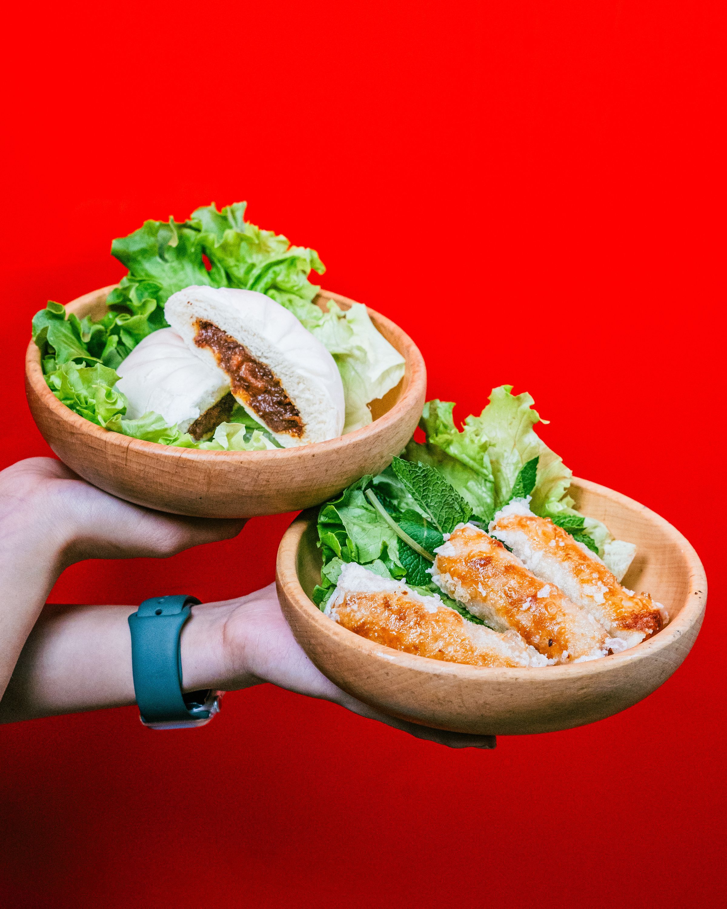 Deux bols en bois contenant des rouleaux de printemps et une brioche à la viande, garnis de salade.