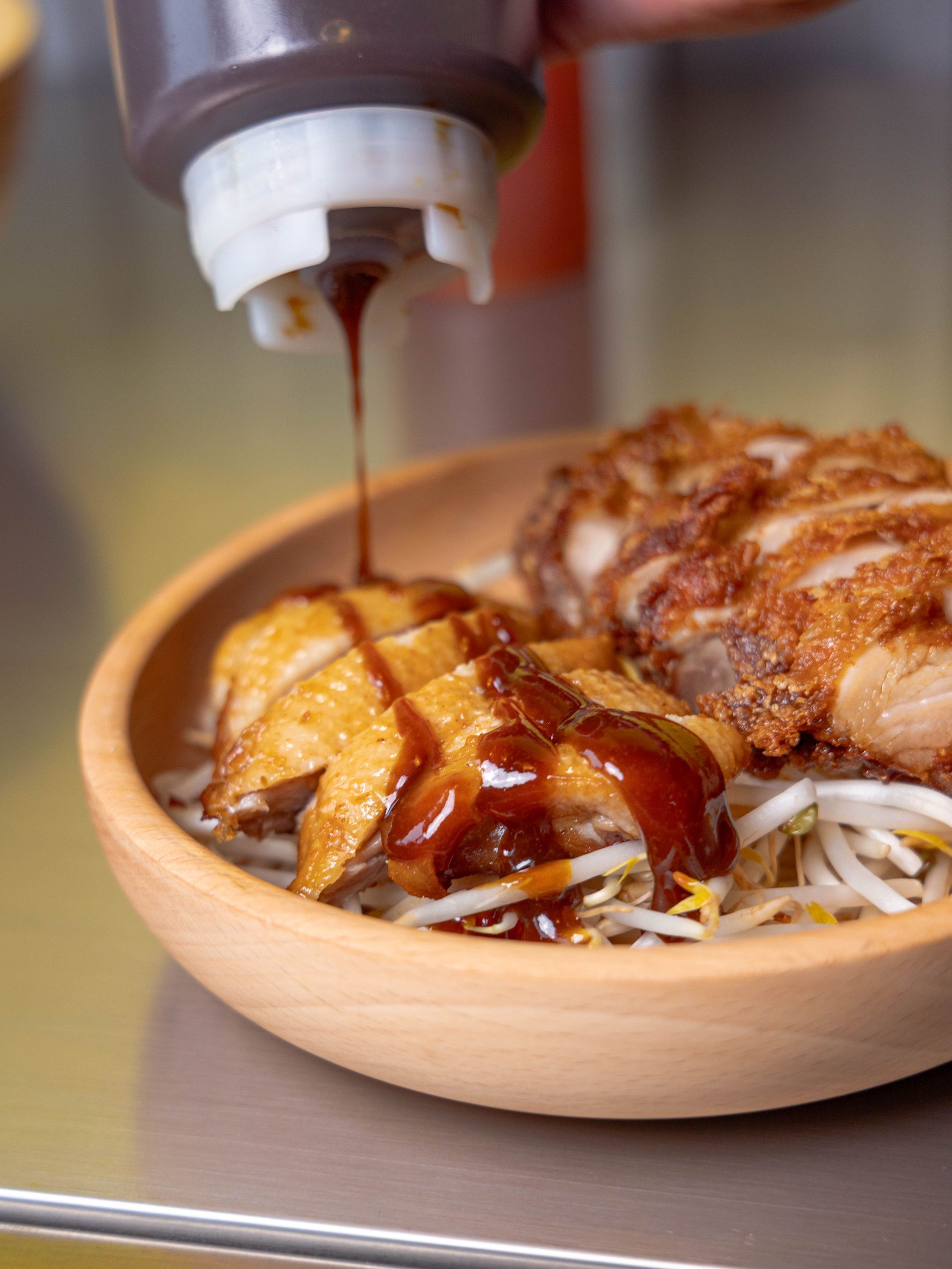 Poulet rôti croustillant avec sauce versée sur un lit de pousses de soja dans un bol en bois.