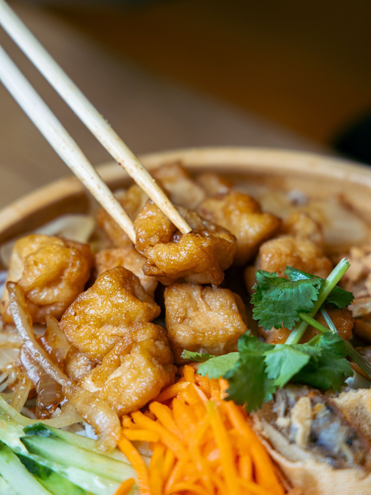 Plat asiatique avec morceaux frits, carottes râpées, concombres et coriandre fraîche dans un bol.