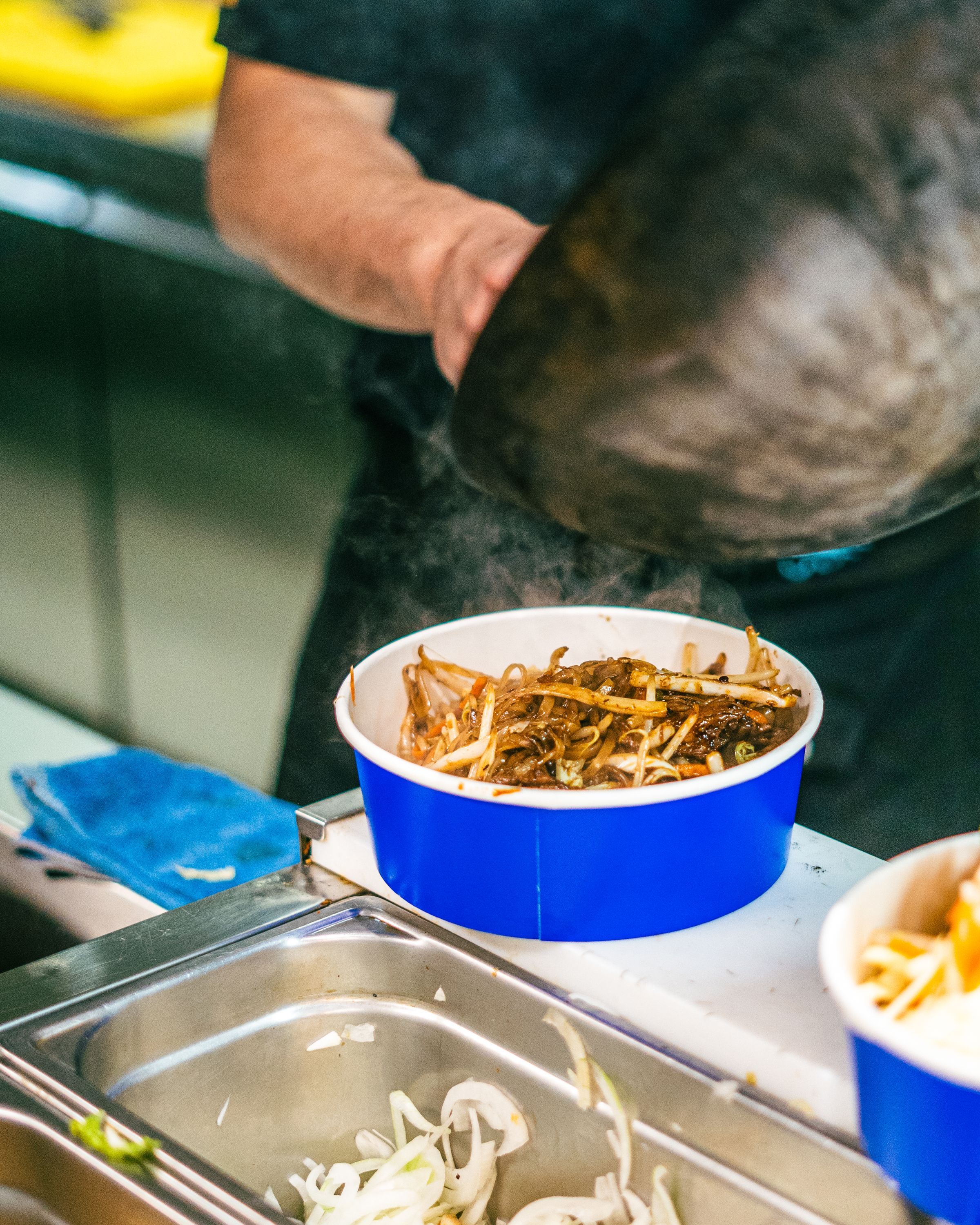 Un plat de nouilles servi dans un récipient bleu, préparé dans un restaurant asiatique de street food.