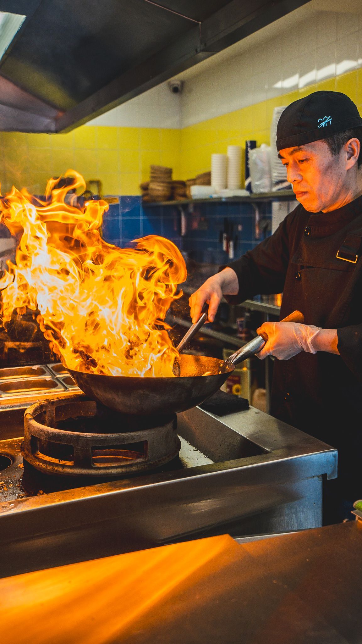 Un chef cuisine avec une poêle flamboyante dans un restaurant asiatique de street food.
