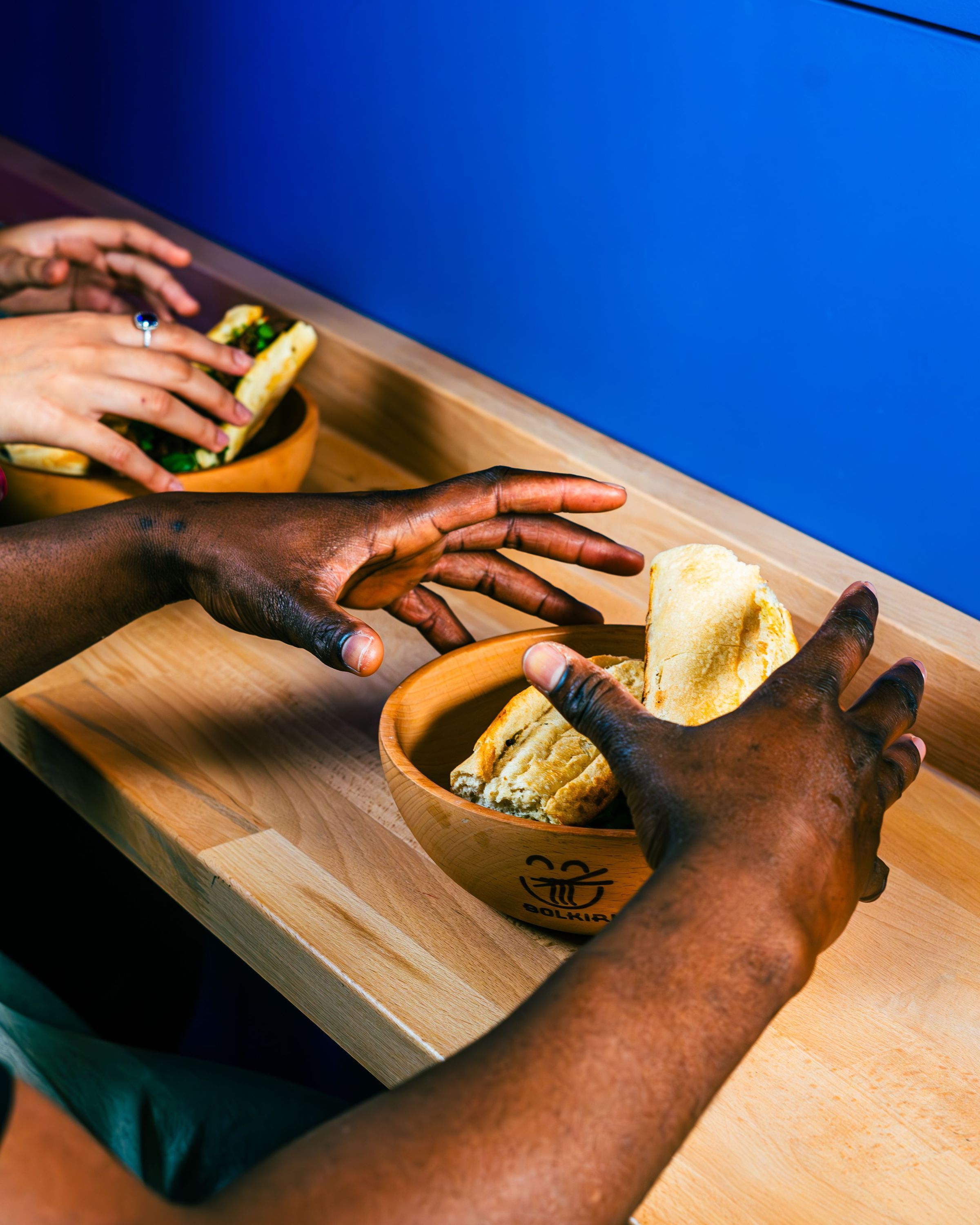 Duo de mains autour d'un bol en bois contenant des mets asiatiques dans un cadre moderne.