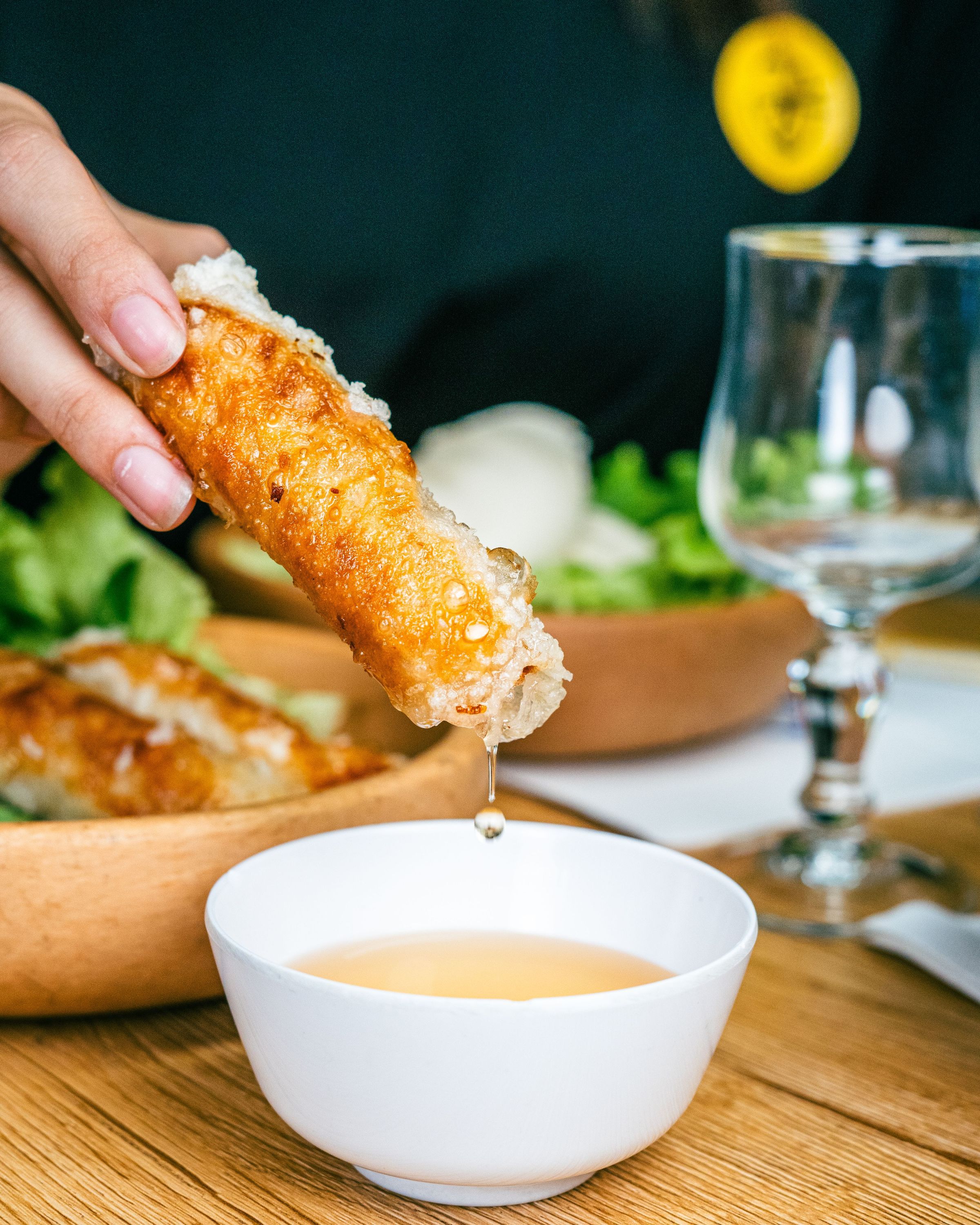 Nems croustillants trempés dans une sauce, servis dans un restaurant asiatique, sur une table en bois.