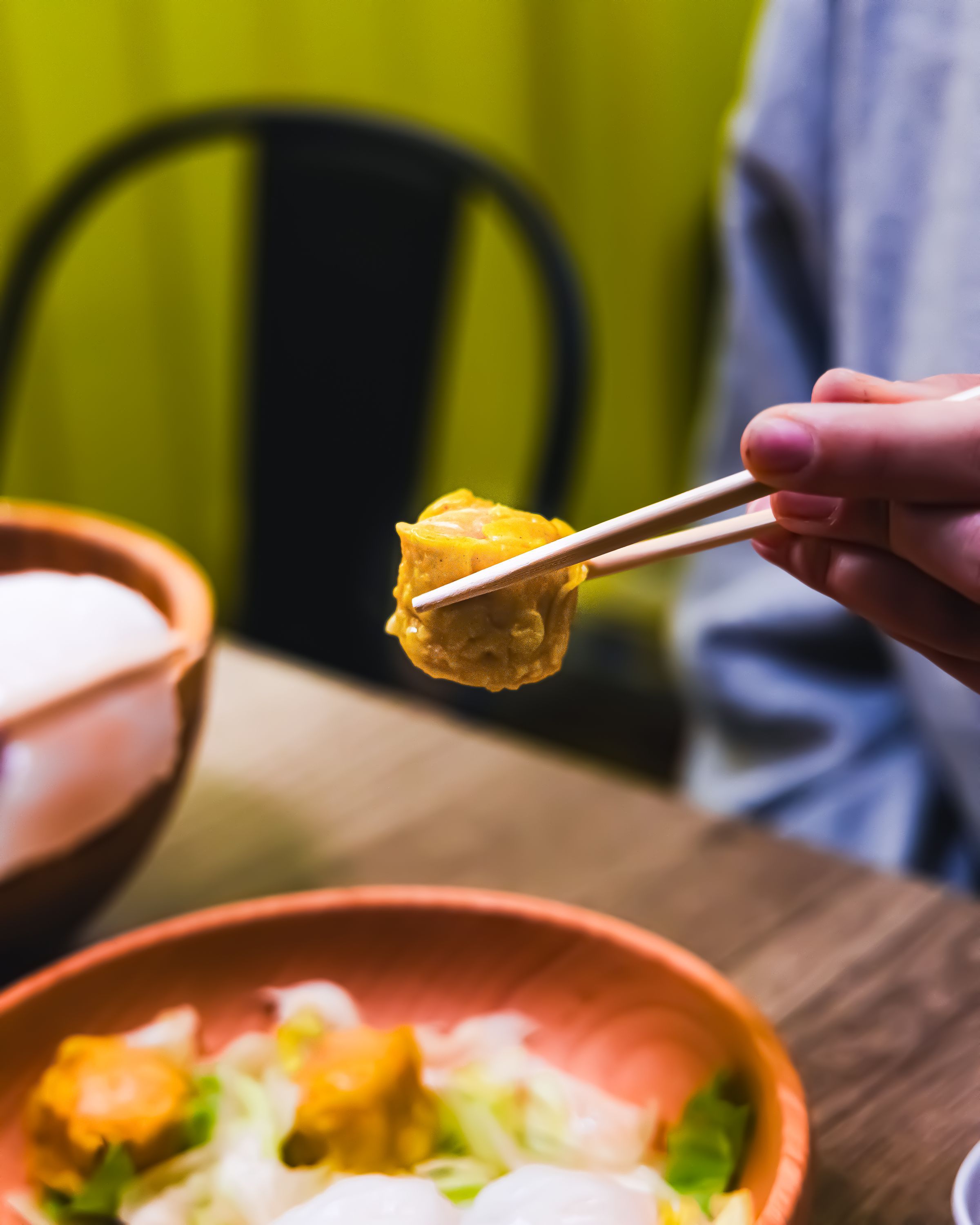 Dumpling saisi avec des baguettes, accompagné d'un plat dans un restaurant asiatique spécialisé en cuisine vietnamienne.