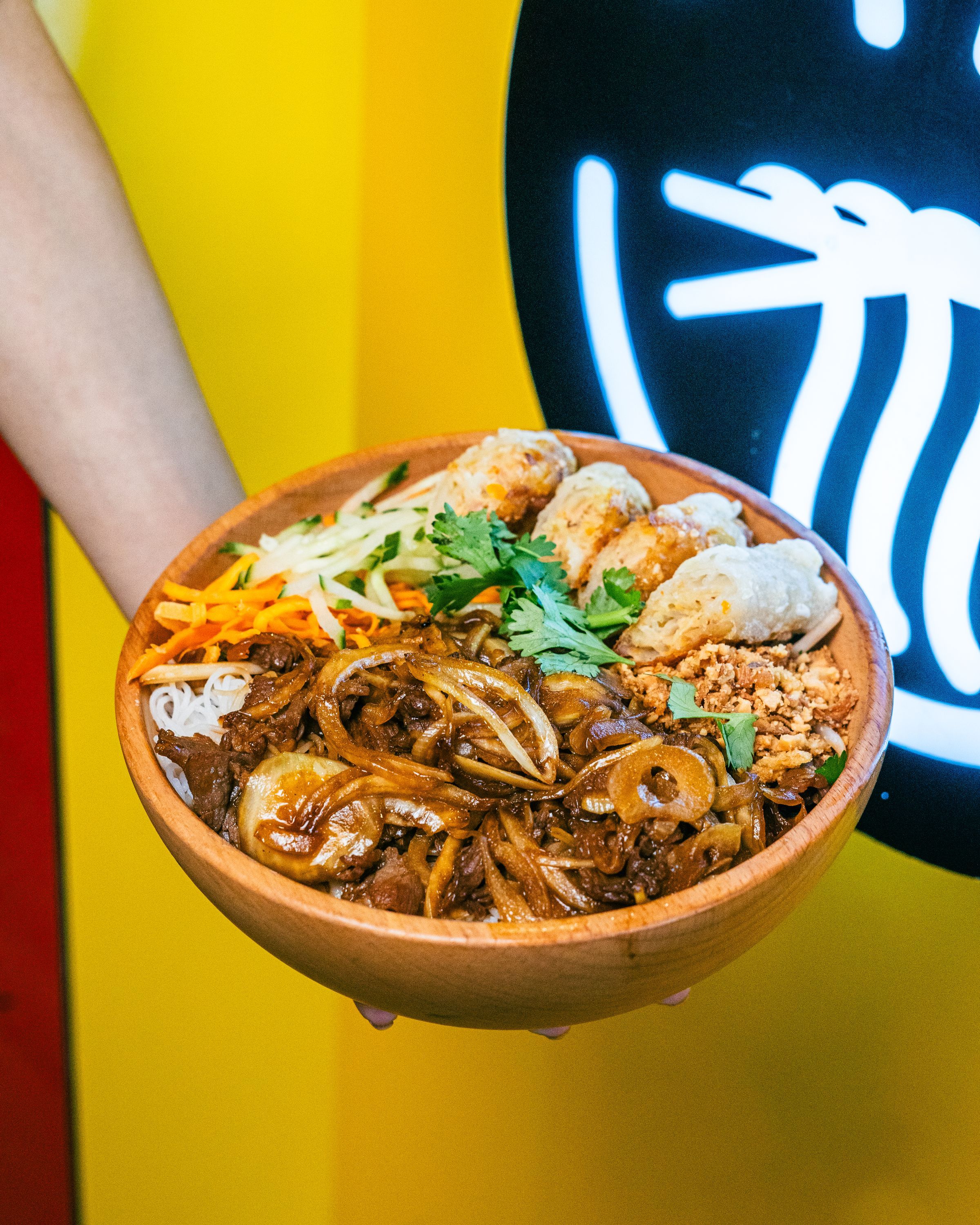 Plat de nouilles vietnamiennes, viande, légumes croquants et nems, type street food, ambiance asiatique.