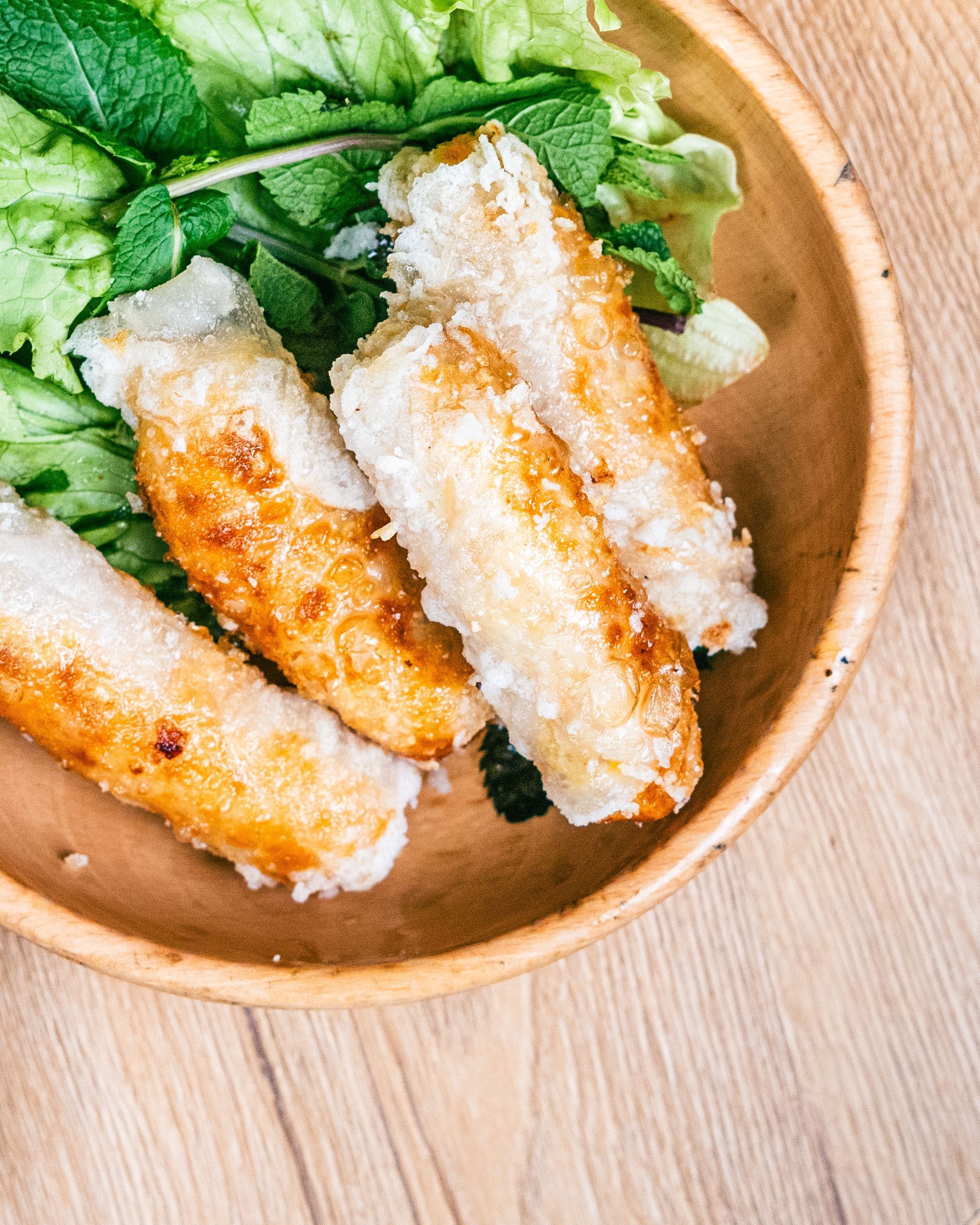 Rouleaux de printemps croustillants servis avec de la salade et de la menthe dans un bol en bois.