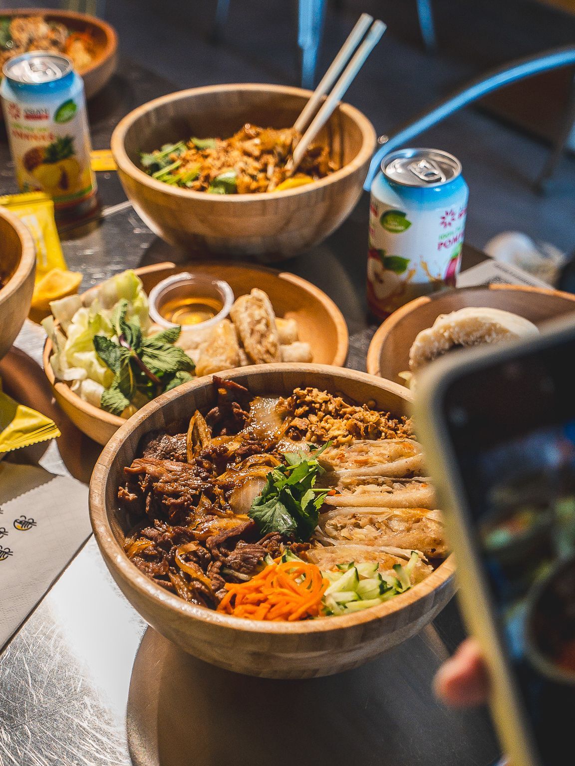 Bol de cuisine vietnamienne avec viande, légumes et garnitures, accompagné de boissons et d'autres plats.